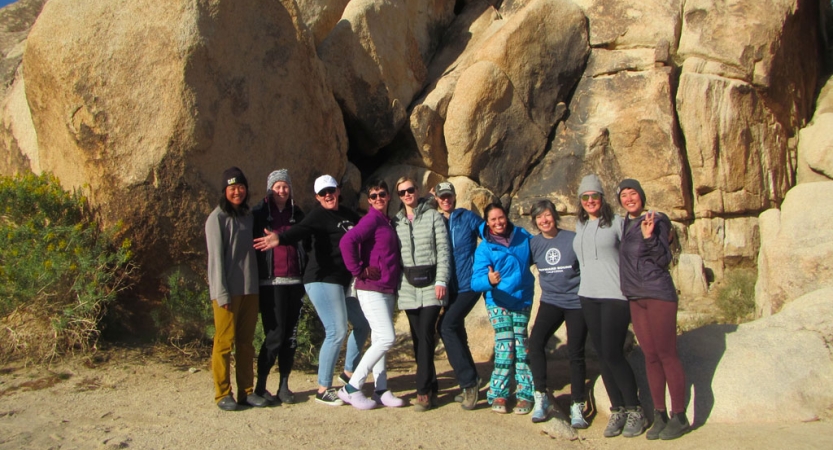 a group of veterans pose for a photo in front of a large rock wall in joshua tree